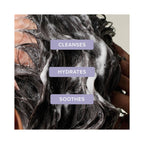Close-up of dark, hair being washed with  text reading 'CLEANSES', 'HYDRATES', and 'SOOTHES'.
