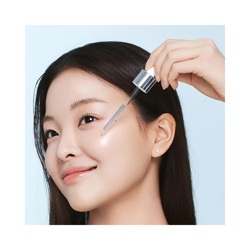 A close-up of a woman applying skincare serum with a silver dropper to her cheek thumbnail 3